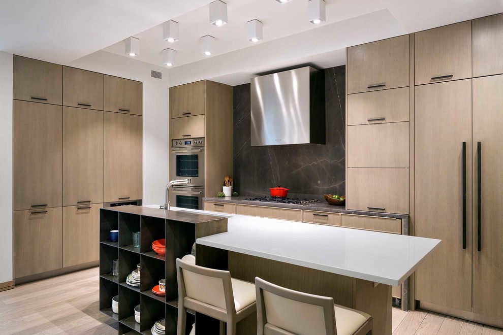 This is an example of a contemporary kitchen in New York with flat-panel cabinets, light wood cabinets, black splashback, panelled appliances, light hardwood floors and with island.