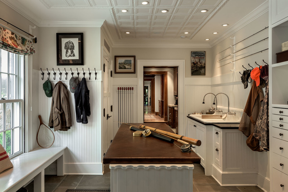 Photo of a mid-sized country single-wall utility room in New York with white walls, slate floors, a drop-in sink, flat-panel cabinets, white cabinets, granite benchtops, a side-by-side washer and dryer and beige floor.