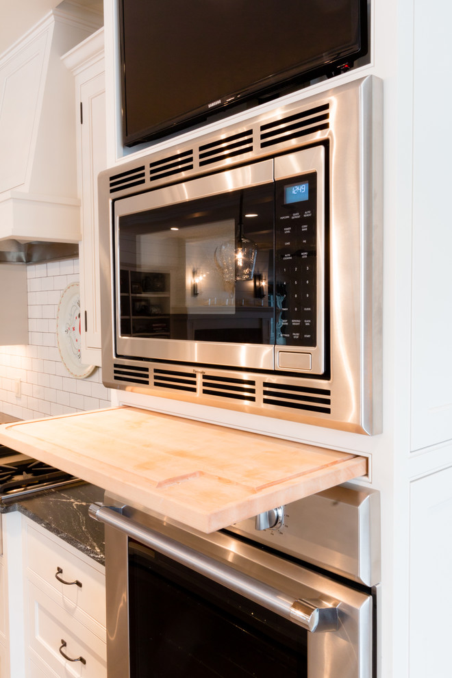 Example of a large transitional l-shaped light wood floor open concept kitchen design in Minneapolis with a farmhouse sink, beaded inset cabinets, white cabinets, granite countertops, white backsplash, subway tile backsplash, stainless steel appliances and an island
