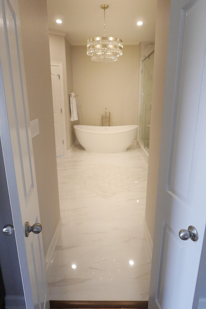 Example of a large transitional master white tile and porcelain tile porcelain tile and white floor freestanding bathtub design with shaker cabinets, white cabinets, a two-piece toilet, beige walls, an undermount sink, marble countertops, a hinged shower door and white countertops
