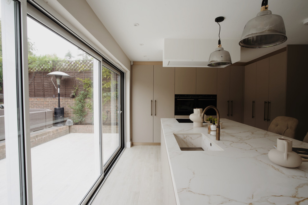 Photo of a medium sized modern l-shaped enclosed kitchen in London with a built-in sink, flat-panel cabinets, beige cabinets, quartz worktops, light hardwood flooring, an island, beige floors and beige worktops.
