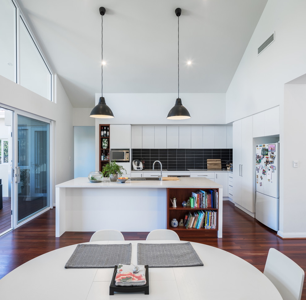 Inspiration for a contemporary l-shaped open plan kitchen in Perth with flat-panel cabinets, white cabinets, black splashback, subway tile splashback, stainless steel appliances, medium hardwood floors, with island and brown floor.