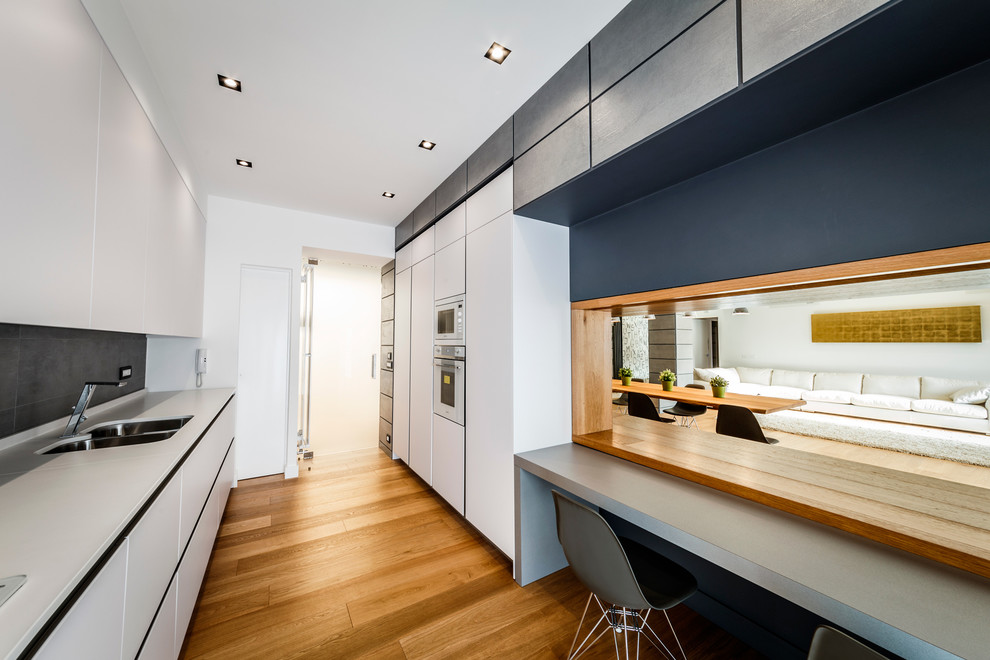 Photo of a mid-sized contemporary galley kitchen in Rome with a double-bowl sink, flat-panel cabinets, white cabinets, grey splashback, white appliances, medium hardwood floors, no island, solid surface benchtops and ceramic splashback.