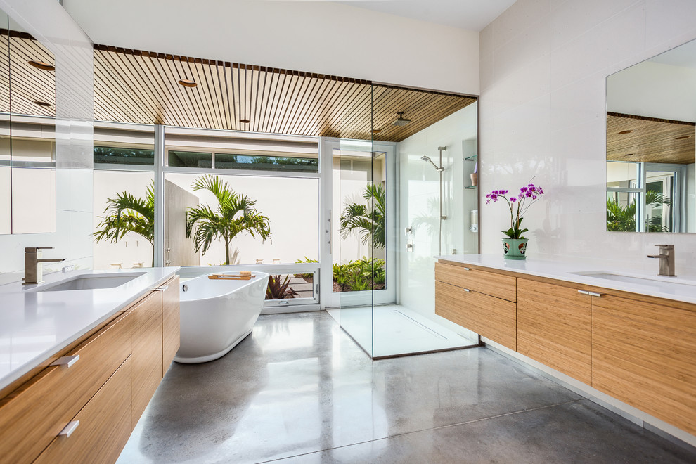 Inspiration for a tropical master bathroom in Tampa with an undermount sink, flat-panel cabinets, medium wood cabinets, engineered quartz benchtops, a freestanding tub, a curbless shower, white tile, concrete floors, beige walls and grey floor.