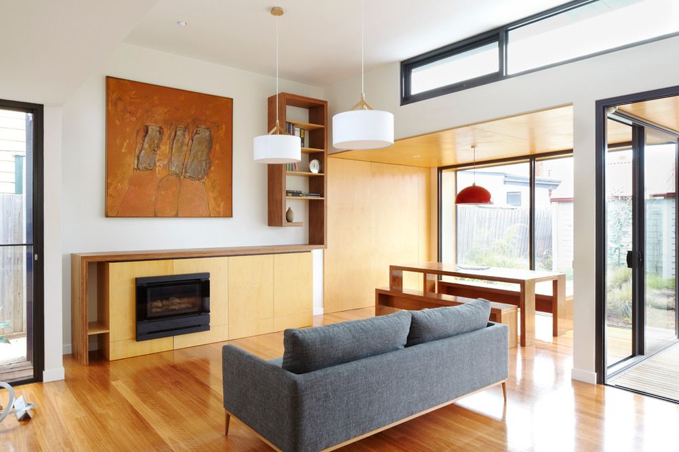 This is an example of a mid-sized modern open concept family room in Melbourne with white walls, medium hardwood floors, a standard fireplace, a wood fireplace surround and a concealed tv.