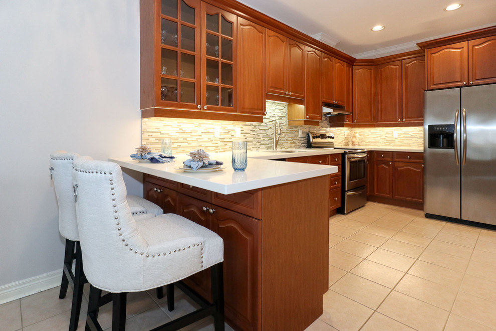 Inspiration for a mid-sized transitional u-shaped porcelain tile and beige floor enclosed kitchen remodel in Toronto with an undermount sink, recessed-panel cabinets, brown cabinets, quartz countertops, beige backsplash, mosaic tile backsplash, stainless steel appliances and a peninsula