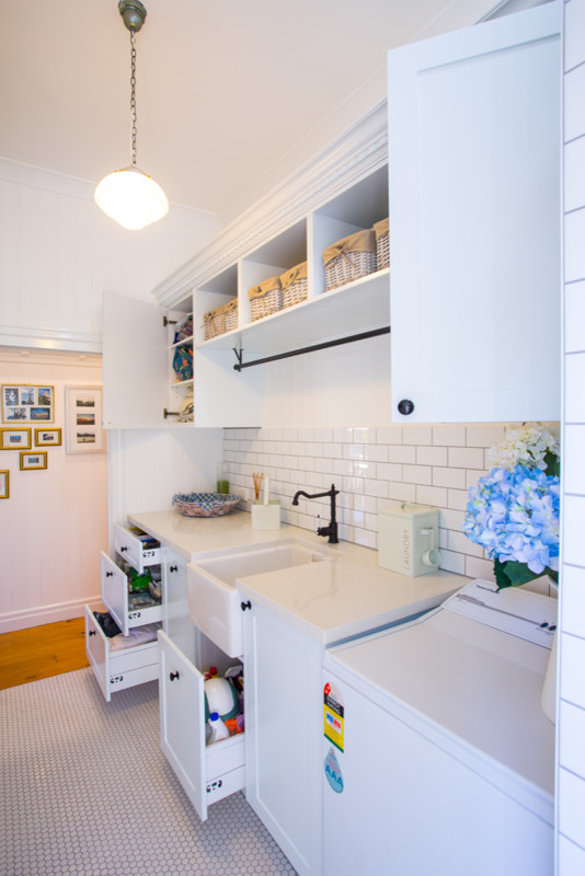 Photo of a mid-sized traditional galley utility room in Brisbane with a farmhouse sink, shaker cabinets, white cabinets, solid surface benchtops, white walls and ceramic floors.
