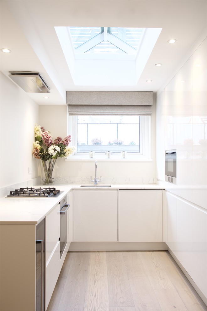 Contemporary u-shaped kitchen in London with an undermount sink, flat-panel cabinets, white cabinets, light hardwood floors, no island and beige floor.