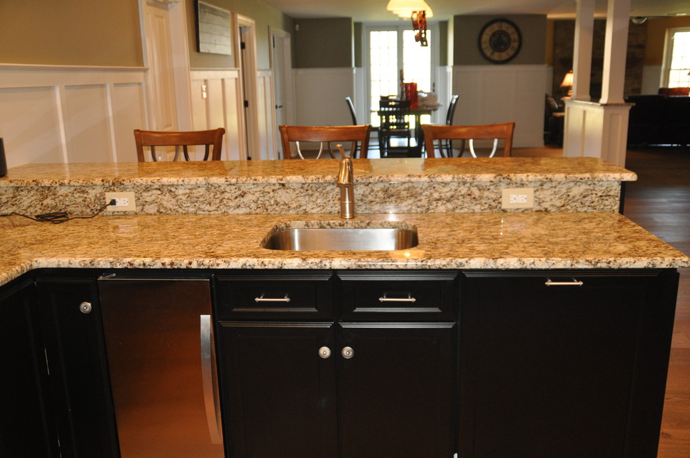This is an example of a mid-sized traditional u-shaped seated home bar in Baltimore with an undermount sink, recessed-panel cabinets, black cabinets, granite benchtops and medium hardwood floors.