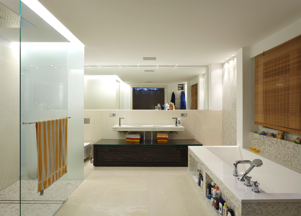 Large contemporary master bathroom in Dusseldorf with an integrated sink, flat-panel cabinets, dark wood cabinets, a drop-in tub, a curbless shower, multi-coloured tile, mosaic tile, beige walls, a wall-mount toilet and limestone floors.