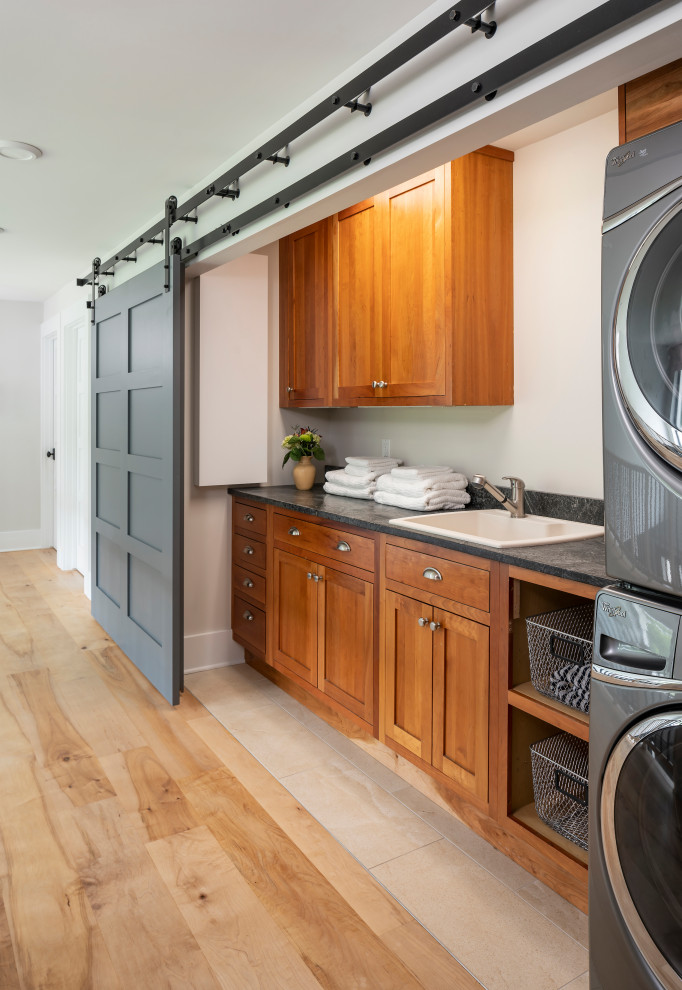 Inspiration for a mid-sized transitional single-wall light wood floor and beige floor dedicated laundry room remodel in Detroit with a drop-in sink, shaker cabinets, medium tone wood cabinets, laminate countertops, white walls, a stacked washer/dryer and gray countertops