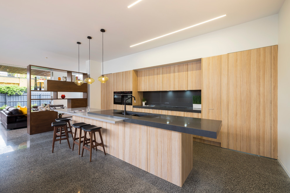Mid-sized contemporary galley open plan kitchen in Melbourne with an undermount sink, flat-panel cabinets, light wood cabinets, black splashback, panelled appliances, with island and concrete floors.