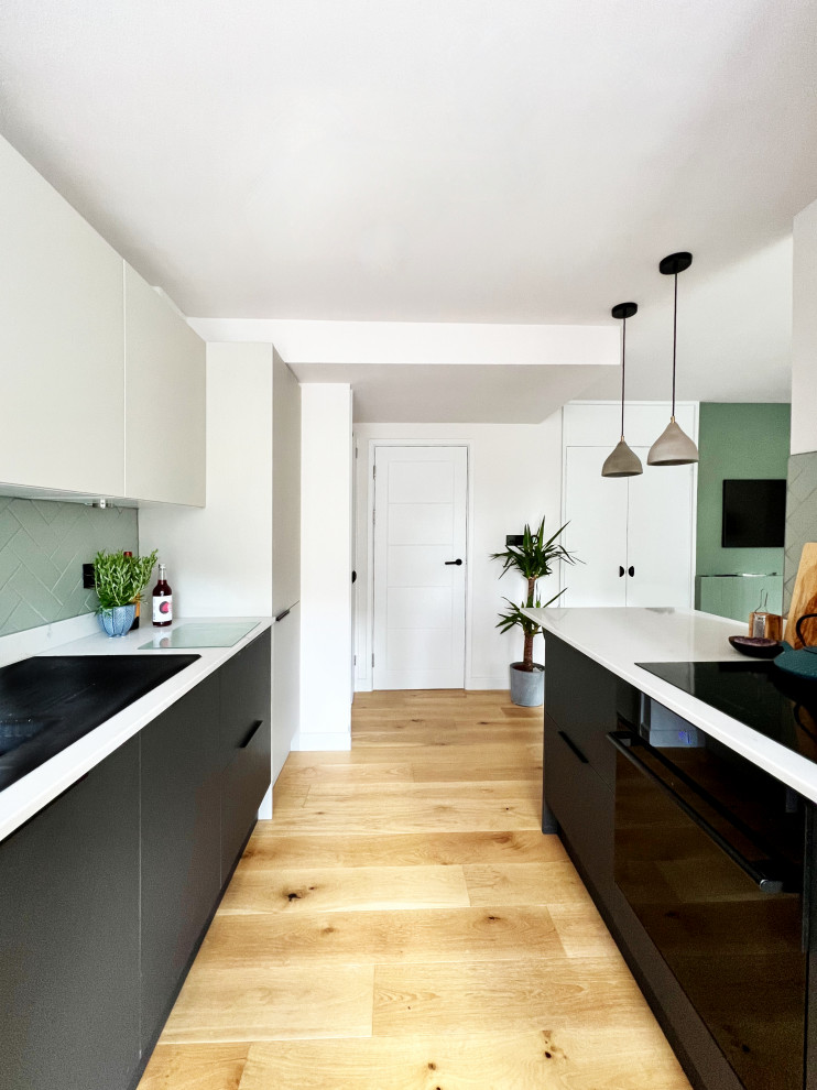 Design ideas for a mid-sized scandinavian galley open plan kitchen in London with a single-bowl sink, flat-panel cabinets, beige cabinets, quartzite benchtops, green splashback, ceramic splashback, black appliances, medium hardwood floors, a peninsula and white benchtop.