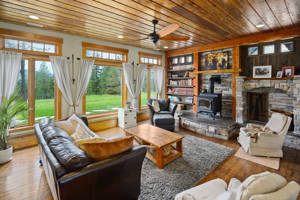 Expansive country open concept living room in Seattle with multi-coloured walls, light hardwood floors, a wood stove, a stone fireplace surround and brown floor.