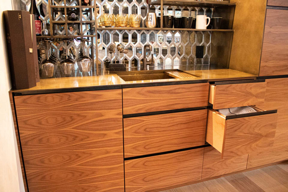Inspiration for a mid-sized contemporary galley wet bar in Other with an integrated sink, flat-panel cabinets, medium wood cabinets, stainless steel benchtops, glass sheet splashback, light hardwood floors, brown floor and yellow benchtop.