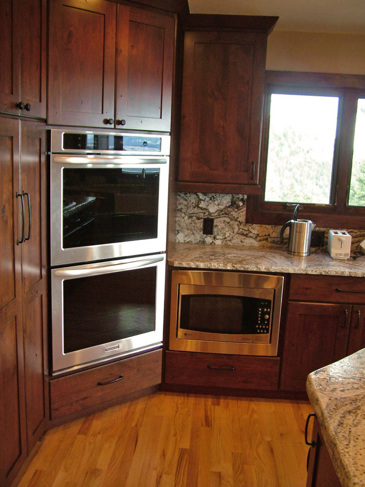 Inspiration for a large rustic u-shaped medium tone wood floor home design remodel in Denver with a farmhouse sink, flat-panel cabinets, dark wood cabinets, granite countertops, gray backsplash, stainless steel appliances and an island