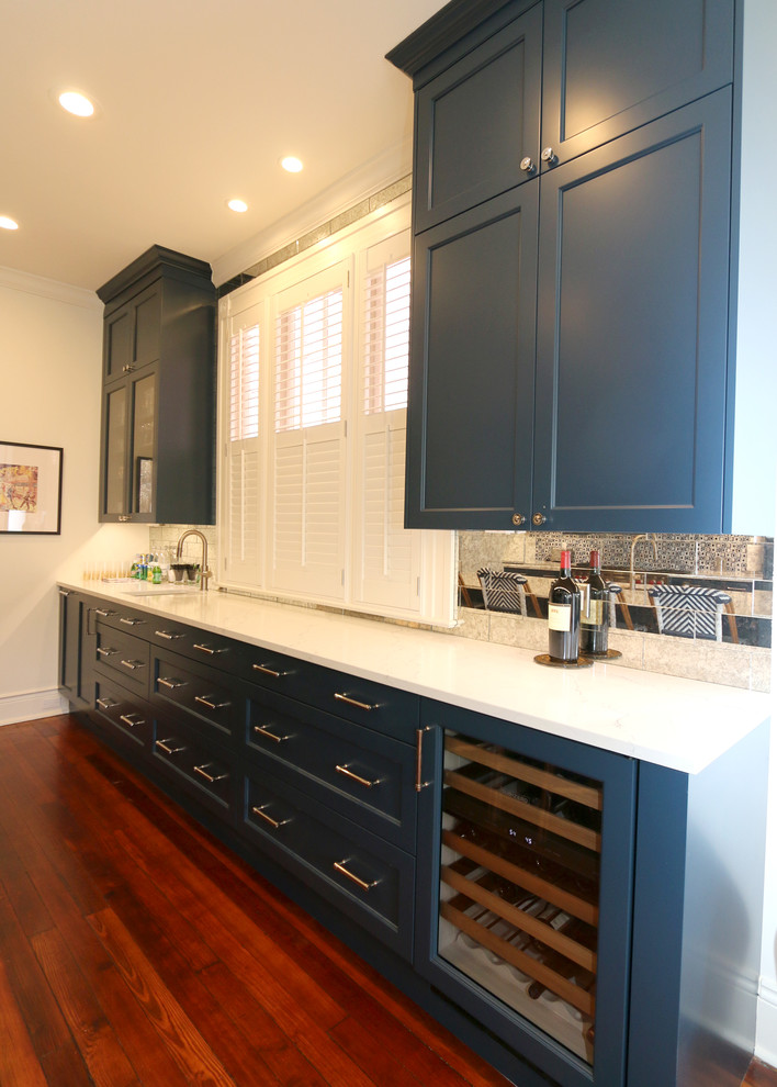 This is an example of a mid-sized transitional kitchen in New Orleans with recessed-panel cabinets, blue cabinets, mirror splashback, medium hardwood floors, with island, brown floor and white benchtop.