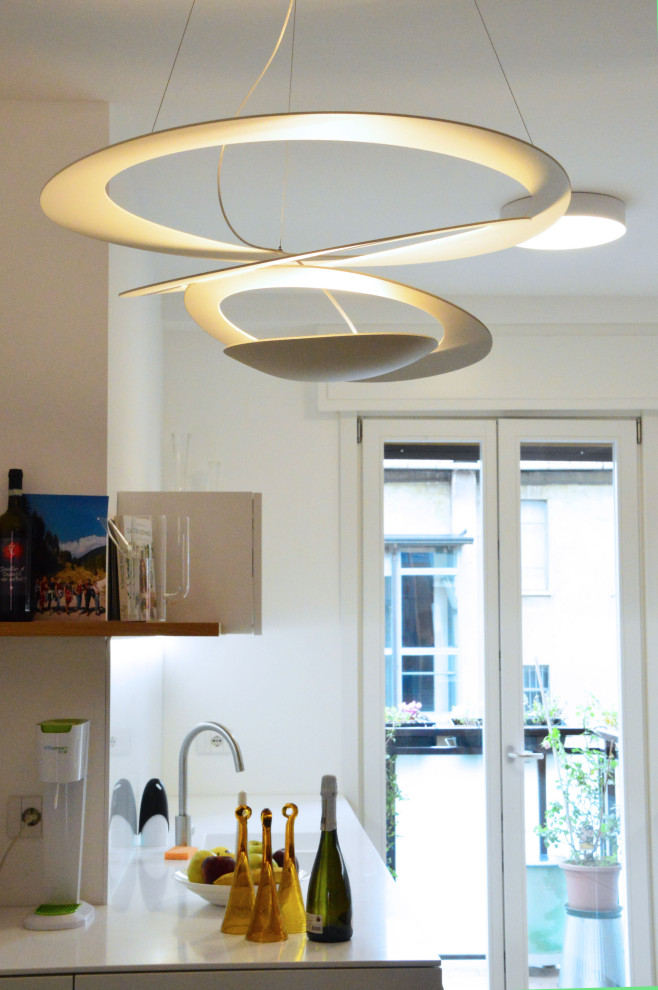 This is an example of a contemporary kitchen in Milan with white cabinets, light hardwood flooring and white worktops.