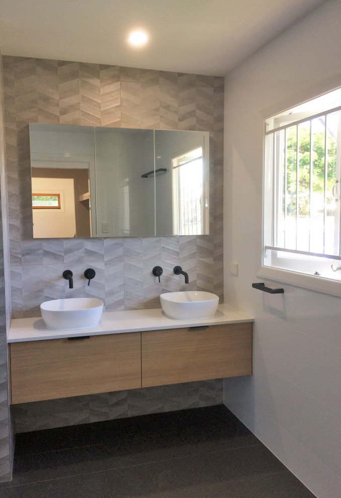 Mid-sized contemporary kids bathroom in Brisbane with flat-panel cabinets, medium wood cabinets, a freestanding tub, an open shower, multi-coloured tile, ceramic tile, black walls, ceramic floors, a vessel sink, engineered quartz benchtops, black floor, an open shower, white benchtops, a niche, a double vanity and a floating vanity.