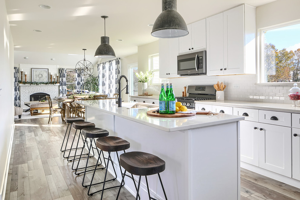 Example of a transitional l-shaped medium tone wood floor and brown floor eat-in kitchen design in Chicago with an undermount sink, shaker cabinets, white cabinets, white backsplash, subway tile backsplash, stainless steel appliances, an island and gray countertops