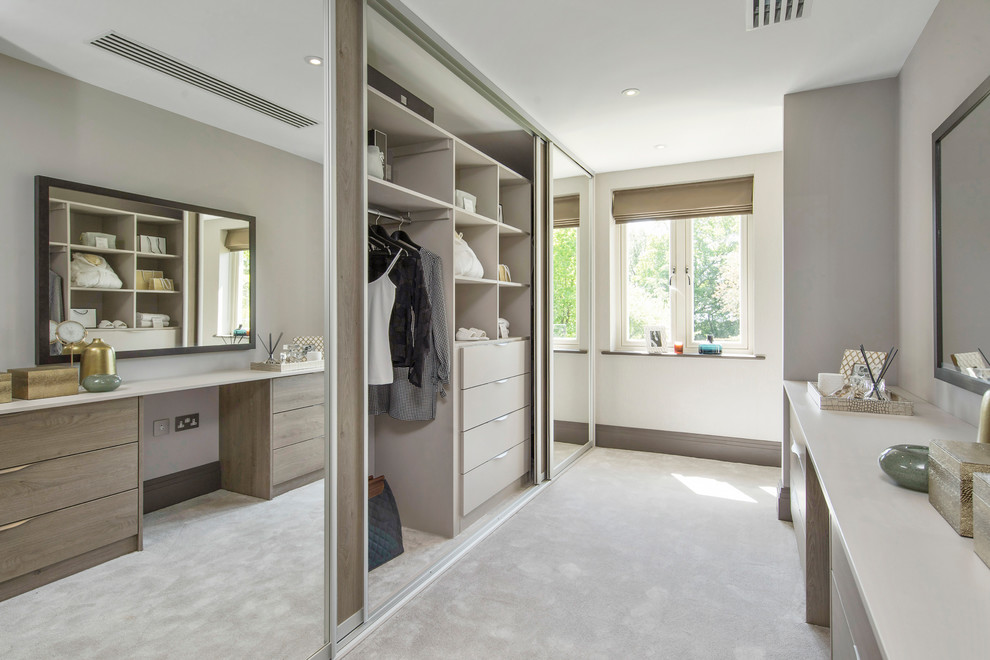 This is an example of a contemporary gender-neutral walk-in wardrobe in London with carpet, flat-panel cabinets, light wood cabinets and beige floor.