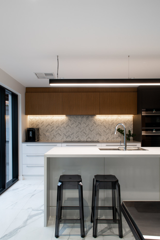 Photo of a mid-sized contemporary kitchen in Adelaide with brown cabinets, solid surface benchtops, grey splashback, ceramic splashback, black appliances, marble floors, with island, grey floor and white benchtop.