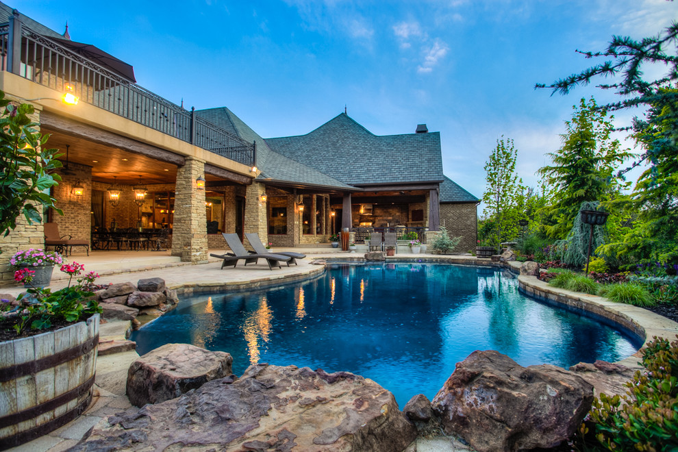 Design ideas for an expansive country backyard custom-shaped pool in Oklahoma City with a water feature and natural stone pavers.