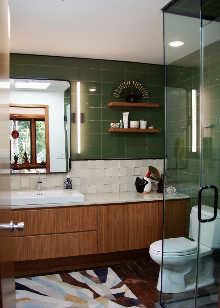 Mid-sized contemporary bathroom in Raleigh with flat-panel cabinets, medium wood cabinets, a corner shower, a one-piece toilet, multi-coloured tile, ceramic tile, multi-coloured walls, brick floors, a vessel sink, engineered quartz benchtops, red floor, a hinged shower door and white benchtops.