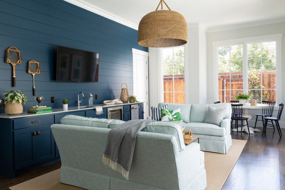 Photo of a large beach style open concept family room in Dallas with a home bar, blue walls, dark hardwood floors, a wall-mounted tv and brown floor.