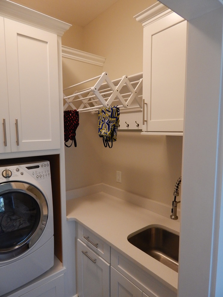 Photo of a large traditional l-shaped laundry room in Charlotte with a farmhouse sink, shaker cabinets, white cabinets, granite benchtops, grey splashback, glass tile splashback and dark hardwood floors.