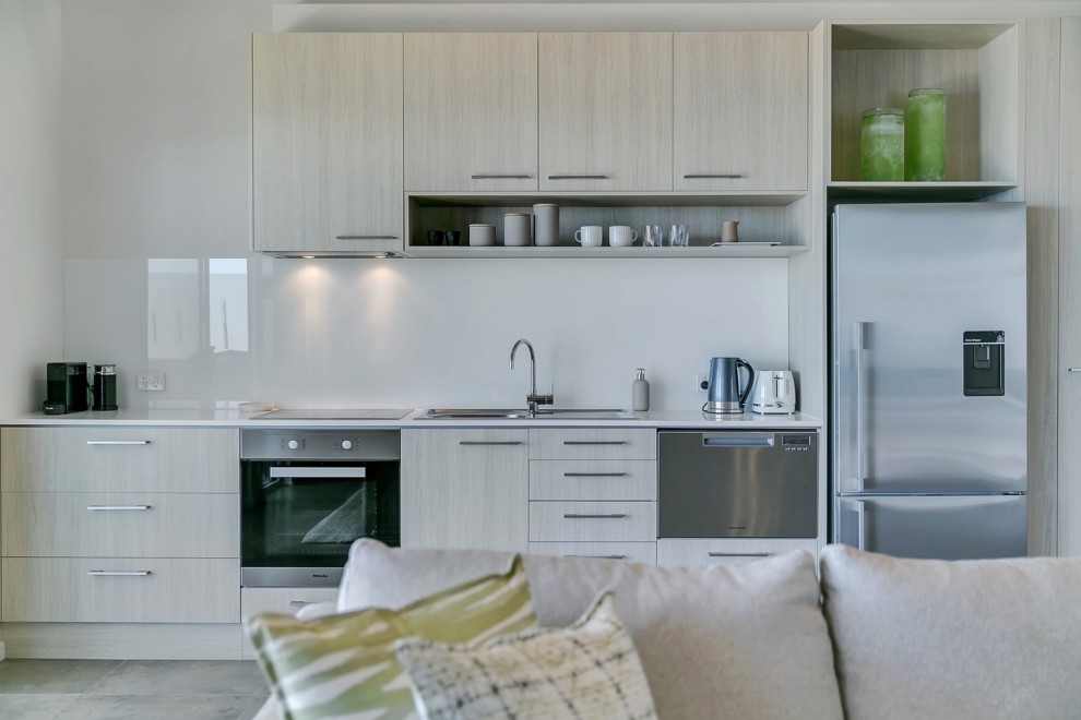 Inspiration for a small contemporary single-wall open plan kitchen in Adelaide with a single-bowl sink, light wood cabinets, engineered stone countertops, white splashback, glass sheet splashback, stainless steel appliances, porcelain flooring, no island, grey floors and white worktops.