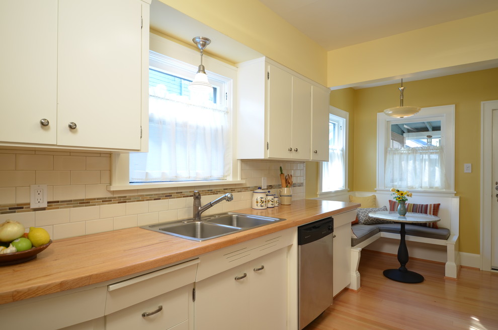 Small arts and crafts galley separate kitchen in Portland with a drop-in sink, flat-panel cabinets, white cabinets, wood benchtops, white splashback, subway tile splashback, stainless steel appliances and light hardwood floors.