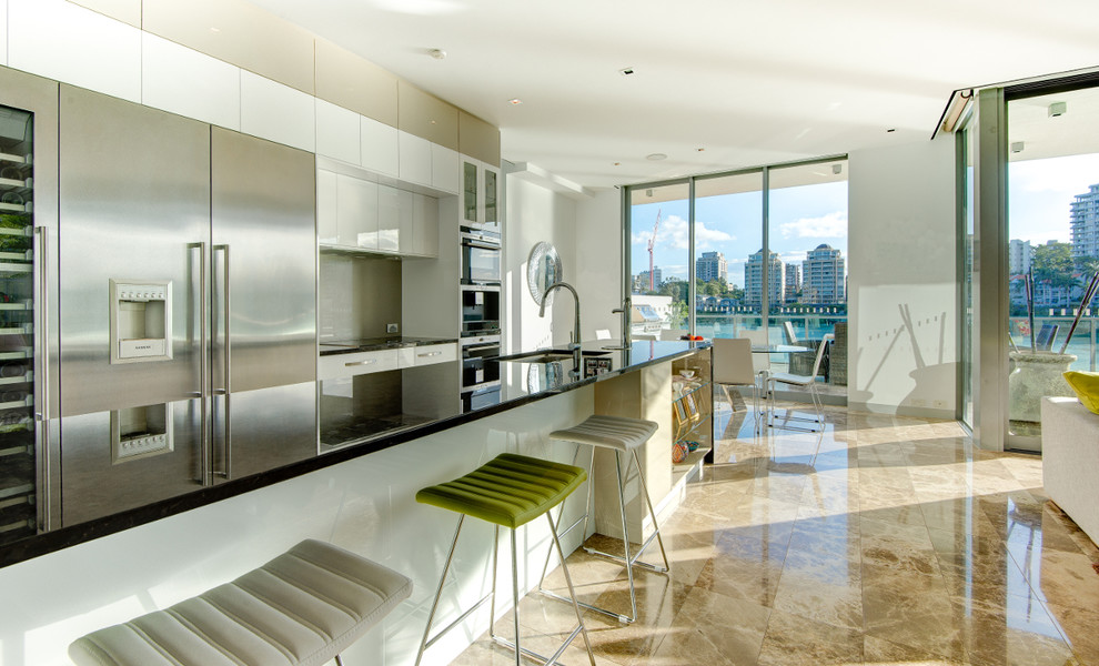 This is an example of a mid-sized contemporary galley open plan kitchen in Brisbane with an undermount sink, flat-panel cabinets, white cabinets, grey splashback, stainless steel appliances, marble benchtops and glass sheet splashback.