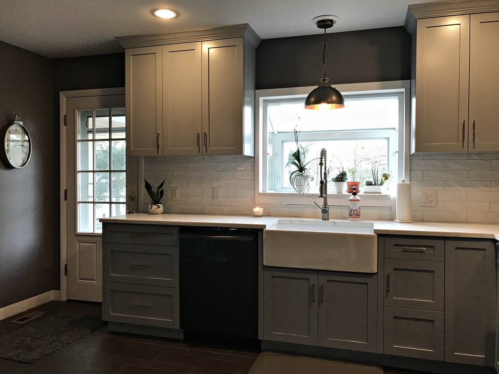Photo of a mid-sized traditional l-shaped kitchen in Philadelphia with a farmhouse sink, shaker cabinets, grey cabinets, marble benchtops, white splashback, subway tile splashback, black appliances, no island, black floor and white benchtop.
