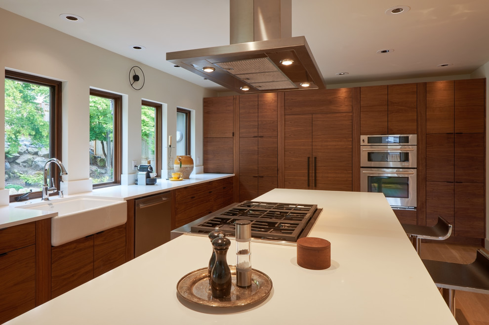 Design ideas for a mid-sized midcentury l-shaped eat-in kitchen in Seattle with a farmhouse sink, flat-panel cabinets, medium wood cabinets, quartz benchtops, white splashback, stainless steel appliances, light hardwood floors and with island.