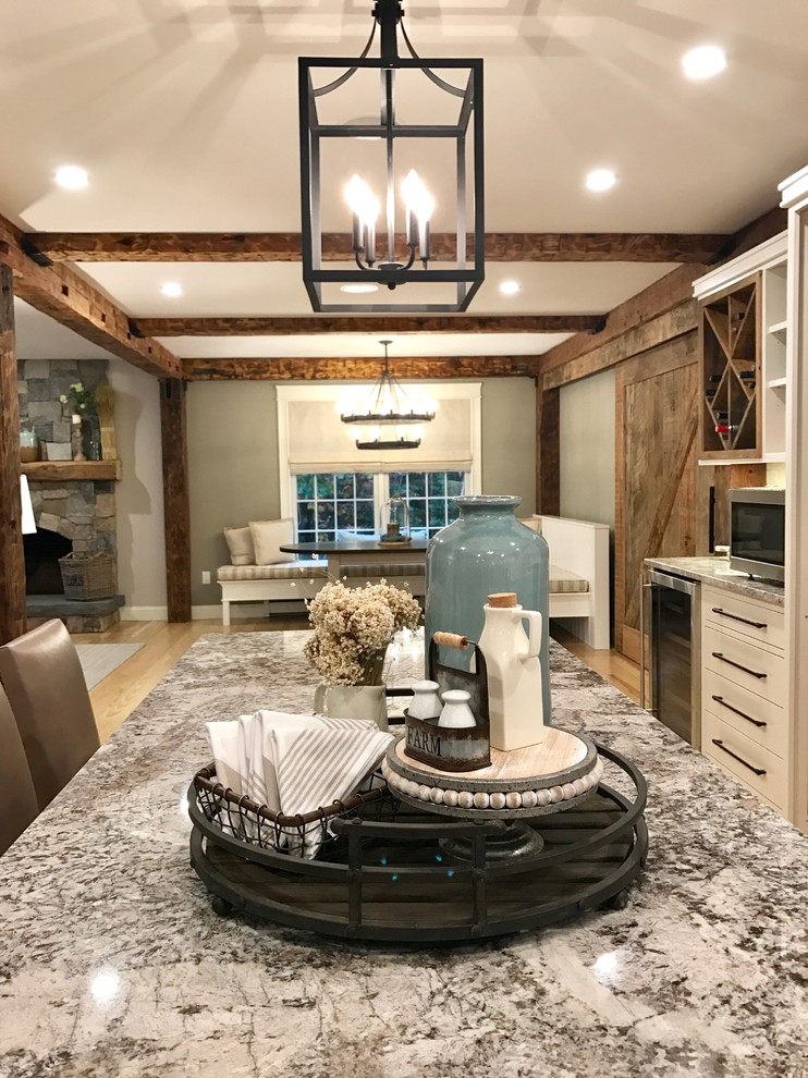 Inspiration for a large country l-shaped eat-in kitchen in Portland Maine with a farmhouse sink, shaker cabinets, white cabinets, granite benchtops, grey splashback, subway tile splashback, stainless steel appliances, light hardwood floors, with island, multi-coloured benchtop and exposed beam.