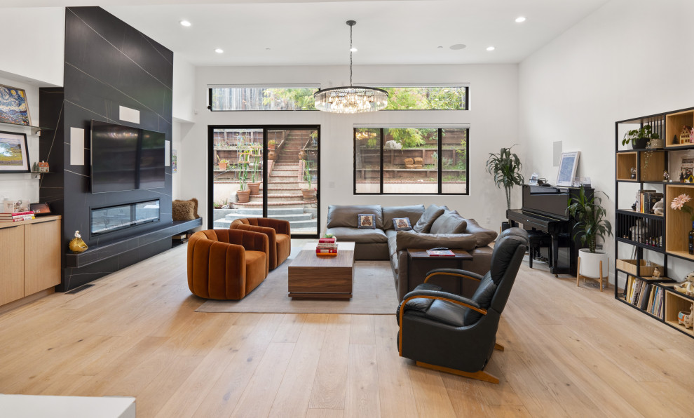 This is an example of a large contemporary open concept family room in San Francisco with white walls, light hardwood floors, no fireplace, a stone fireplace surround, a wall-mounted tv and yellow floor.