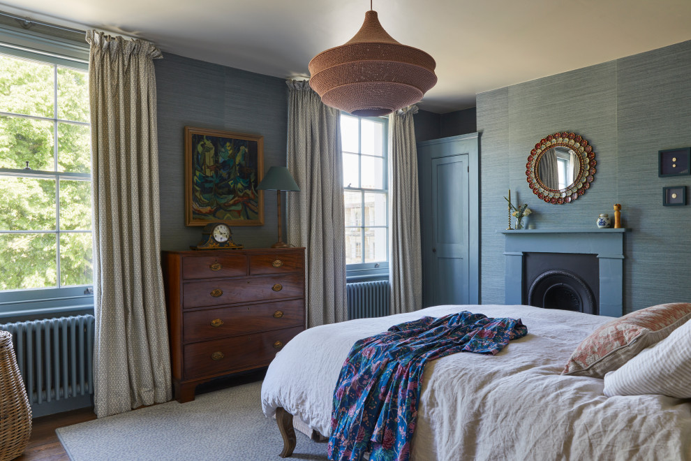 Design ideas for a large traditional master bedroom in London with blue walls, dark hardwood flooring, a standard fireplace, a wooden fireplace surround, brown floors, wallpapered walls and a chimney breast.