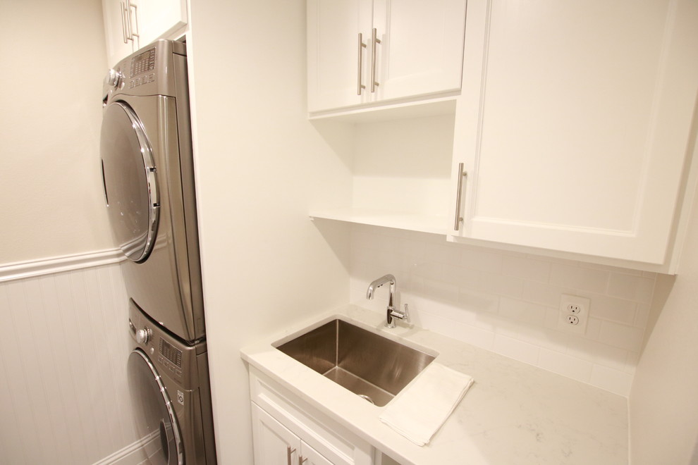 This is an example of a large traditional single-wall dedicated laundry room in Houston with an undermount sink, shaker cabinets, white cabinets, granite benchtops, beige walls, concrete floors, a stacked washer and dryer and grey floor.