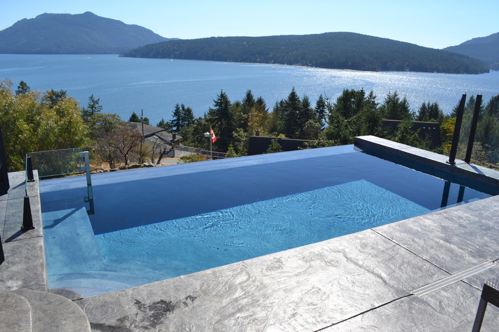 This is an example of a small traditional front yard rectangular infinity pool in Vancouver with a water feature and stamped concrete.