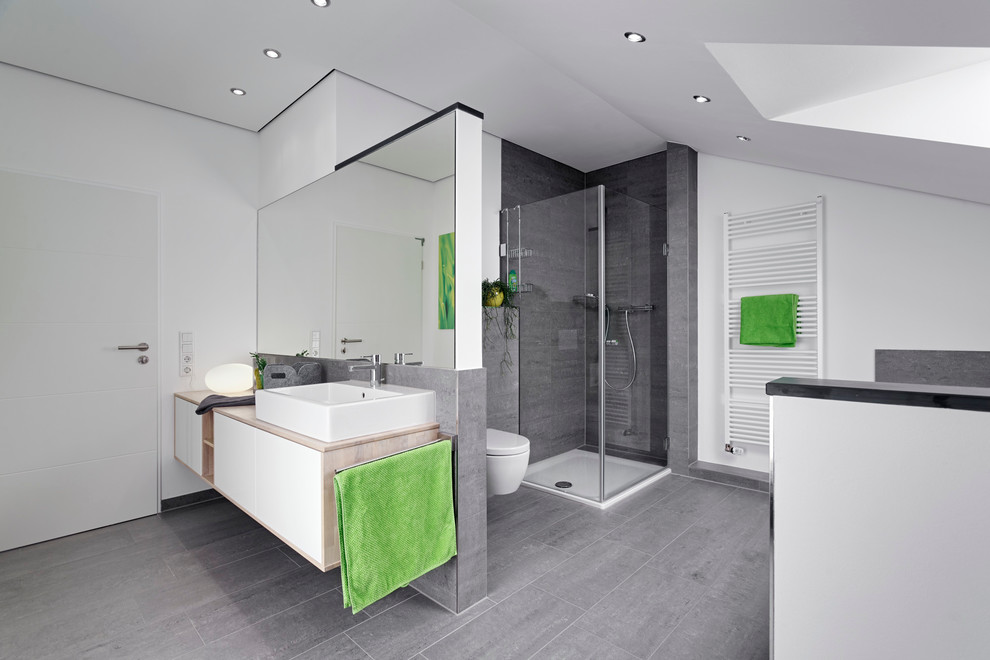 Inspiration for a contemporary 3/4 bathroom in Dortmund with flat-panel cabinets, white cabinets, a corner shower, gray tile, white walls, a vessel sink, a wall-mount toilet, stone tile and wood benchtops.
