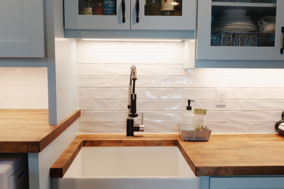 Photo of a large coastal galley utility room in Seattle with a belfast sink, shaker cabinets, blue cabinets, wood worktops, white splashback, ceramic splashback, beige walls, medium hardwood flooring, a side by side washer and dryer, brown floors and brown worktops.