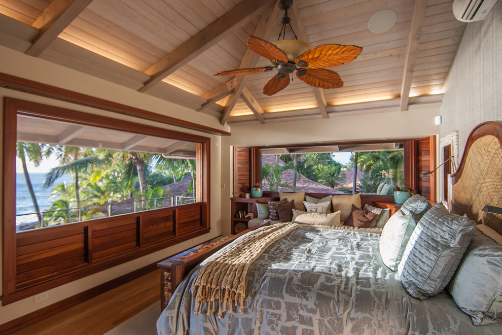 Tropical master bedroom in Hawaii with beige walls, medium hardwood floors and brown floor.