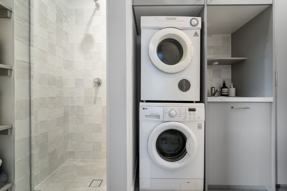 Photo of a mid-sized transitional single-wall utility room in Sydney with a drop-in sink, flat-panel cabinets, grey cabinets, quartz benchtops, ceramic splashback, multi-coloured walls, ceramic floors, an integrated washer and dryer, grey floor and white benchtop.