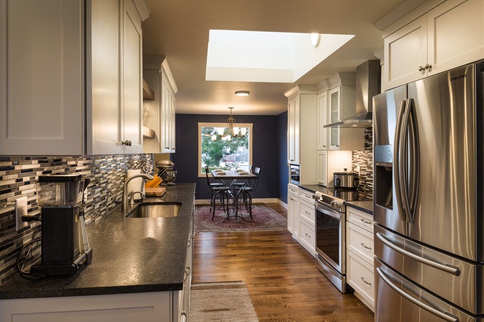 Example of a mid-sized transitional galley medium tone wood floor eat-in kitchen design in Seattle with an undermount sink, shaker cabinets, white cabinets, multicolored backsplash, matchstick tile backsplash, stainless steel appliances and no island