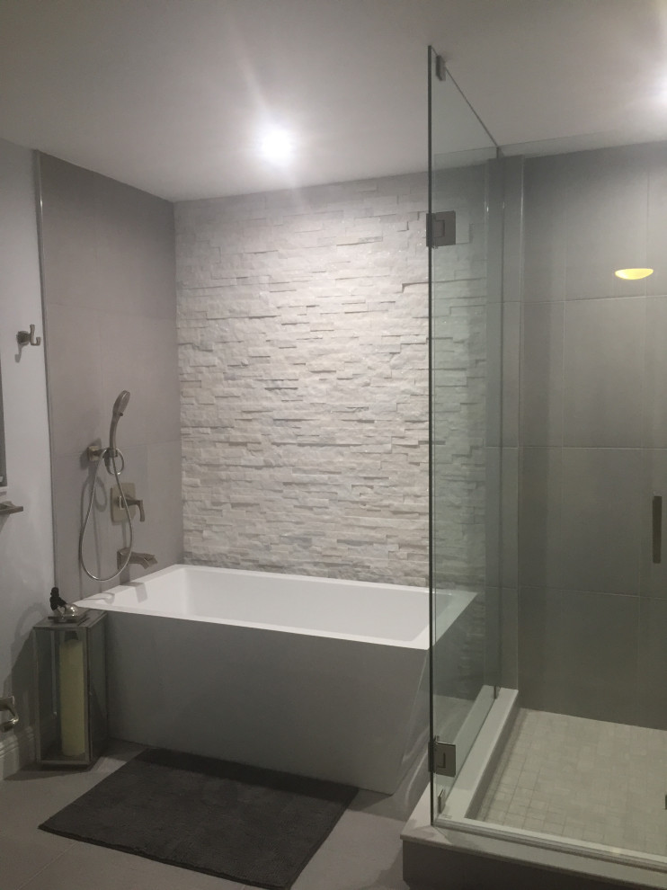 This is an example of a medium sized contemporary grey and white ensuite bathroom in Miami with shaker cabinets, black cabinets, a freestanding bath, a one-piece toilet, grey tiles, stone slabs, grey walls, concrete flooring, a vessel sink, quartz worktops, grey floors, a hinged door, white worktops, a feature wall, double sinks, a freestanding vanity unit and a drop ceiling.