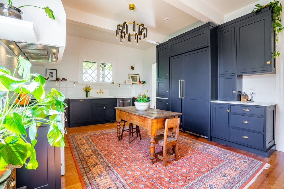 Large eclectic u-shaped separate kitchen in Seattle with a drop-in sink, shaker cabinets, blue cabinets, marble benchtops, white splashback, ceramic splashback, medium hardwood floors, with island, grey benchtop and exposed beam.