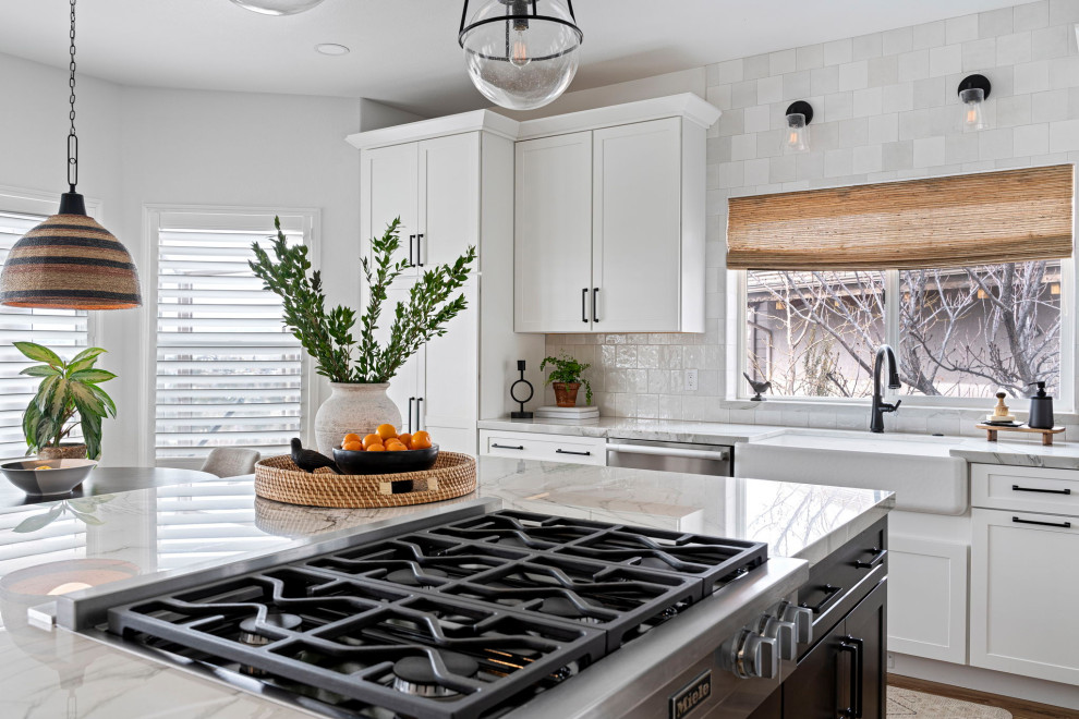 Example of a transitional vinyl floor and brown floor kitchen design with a farmhouse sink, shaker cabinets, white cabinets, quartzite countertops, white backsplash and stainless steel appliances