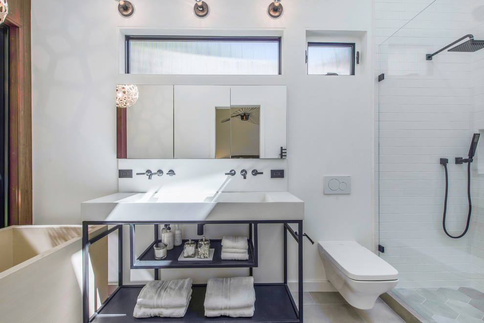 Inspiration for a contemporary bathroom in San Francisco with a freestanding tub, a wall-mount toilet, white tile, subway tile, white walls, a trough sink, grey floor and white benchtops.
