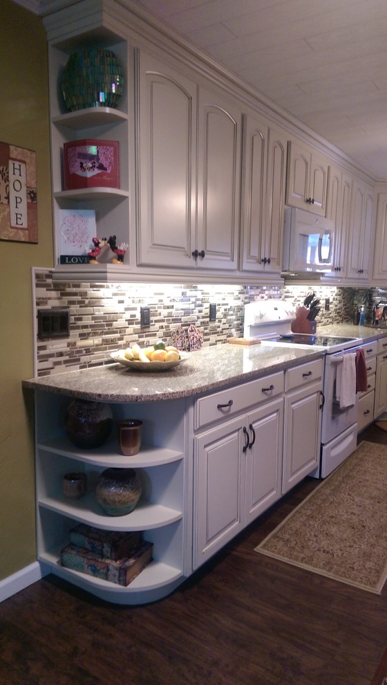 Inspiration for a mid-sized transitional l-shaped laminate floor eat-in kitchen remodel with an undermount sink, raised-panel cabinets, white cabinets, granite countertops, multicolored backsplash, mosaic tile backsplash, white appliances and no island